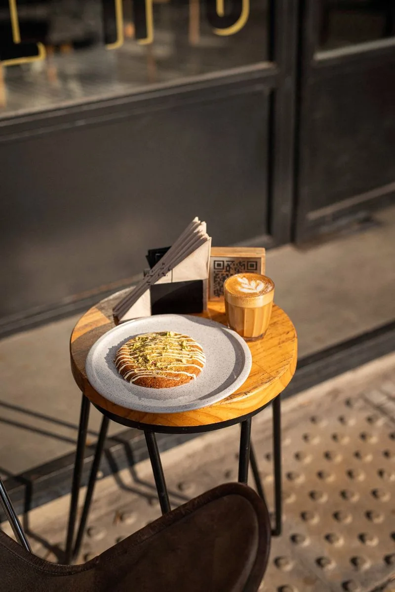 Mesa exterior SĀNTAL Colegiales — carrot cake con pistacho y latte art con luz de invierno dorada