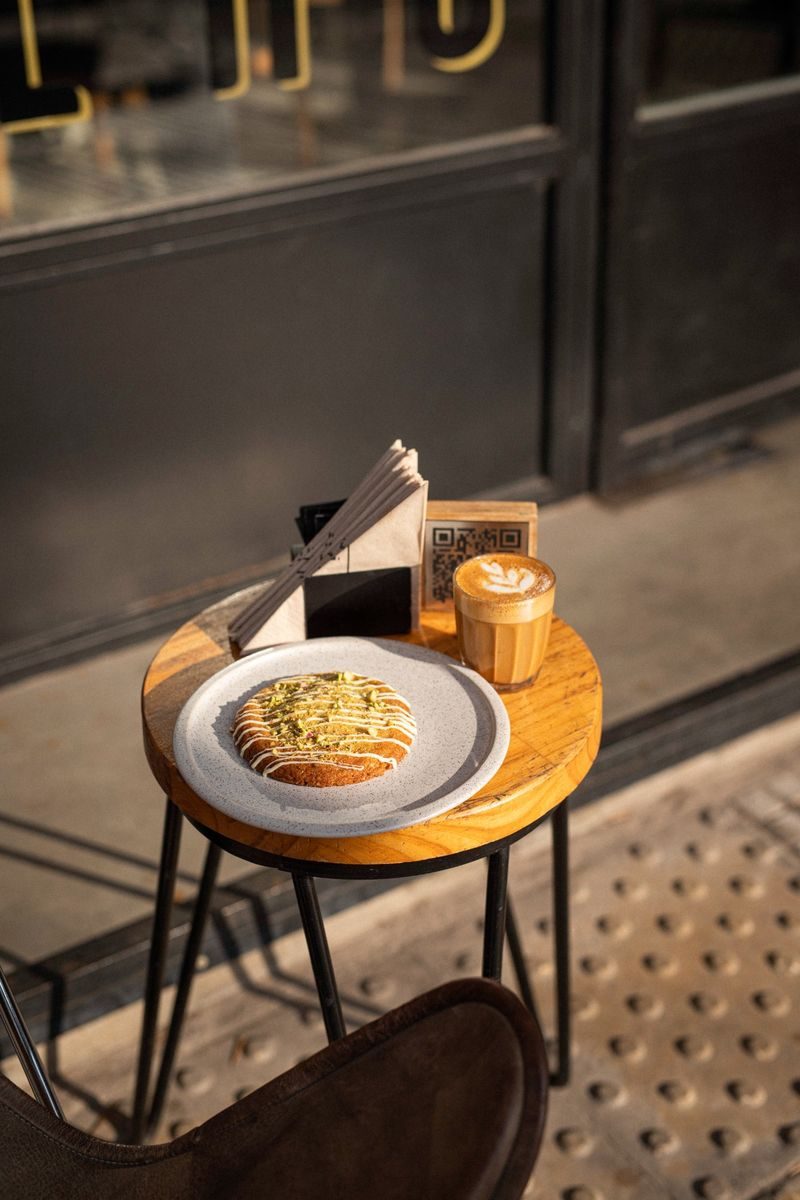 Mesa exterior SĀNTAL Colegiales — carrot cake con pistacho y latte art con luz de invierno dorada